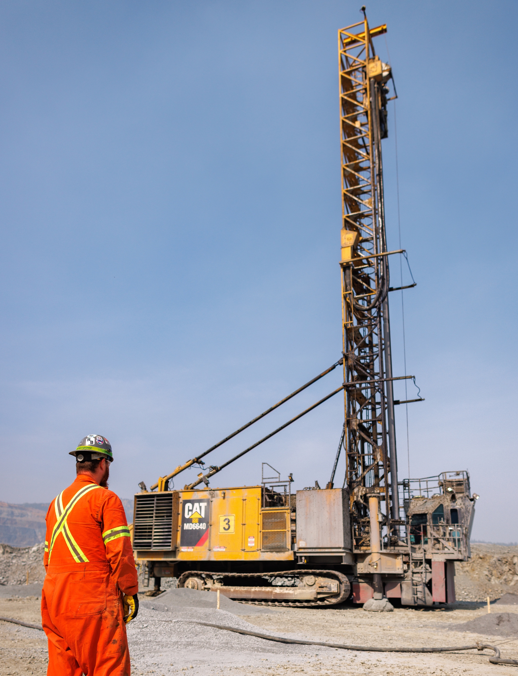 Woman in safety gear smiling outdoors, wearing a hard hat, vest, and glasses.
