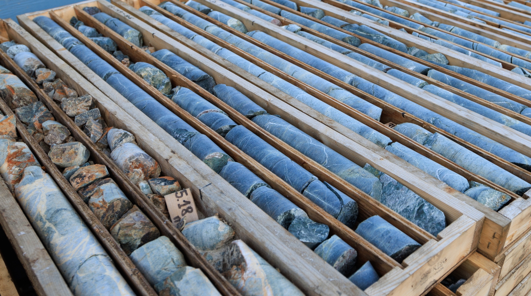 Two workers in safety gear stand behind a colorful geological map, reviewing other maps closely.